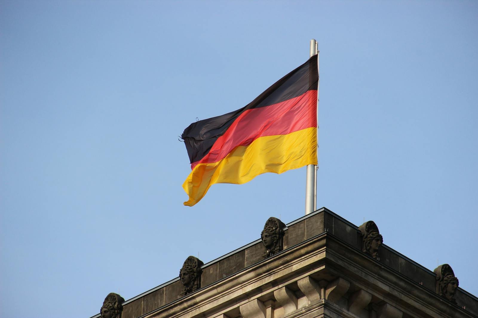 German flag waving on a historic building with blue skies, symbolizing national pride.