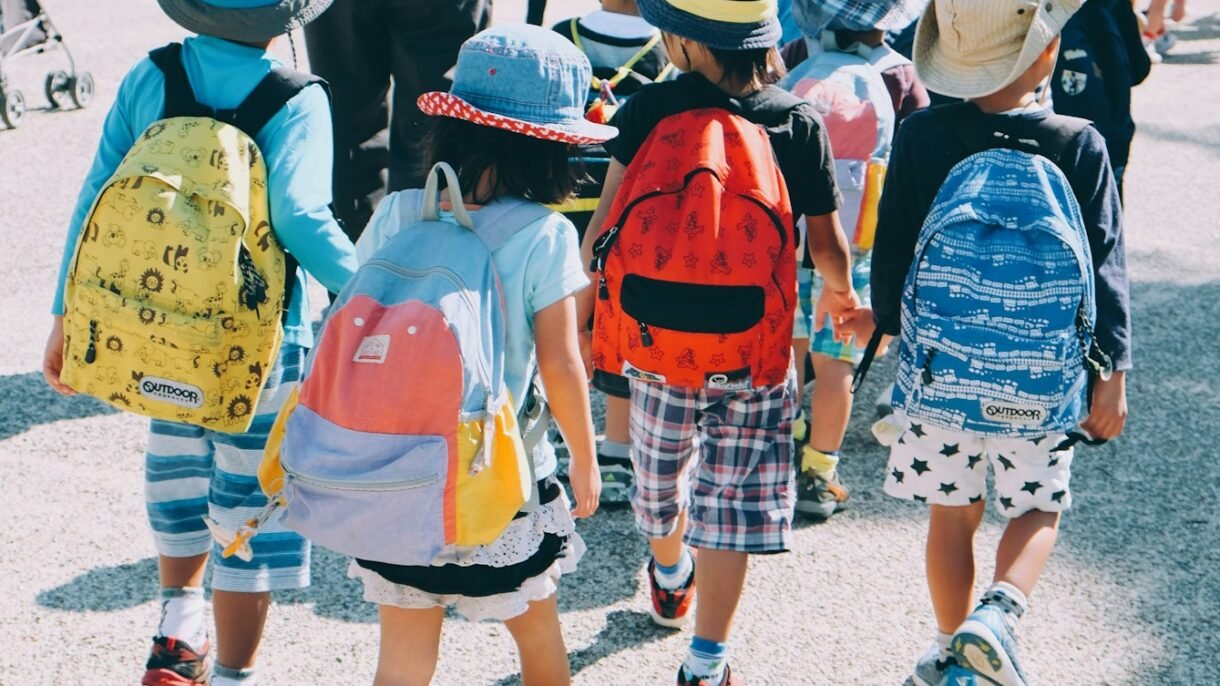 group of people wearing white and orange backpacks walking on gray concrete pavement during daytime