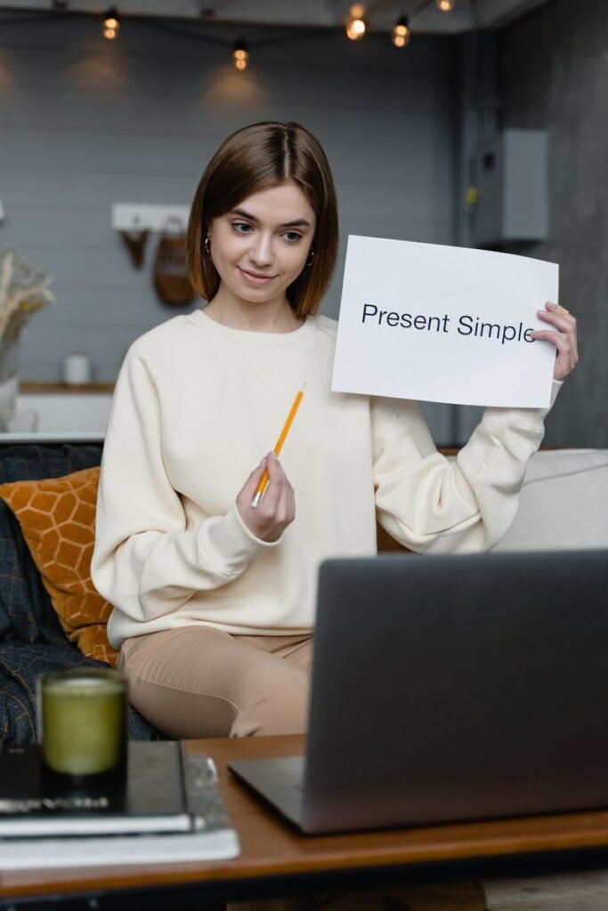 Woman teaching English online holding 'Present Simple' flashcard, engaging in video call.